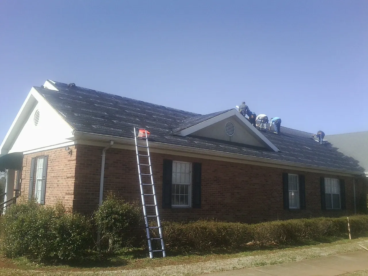 Crew tearing shingles off a brick ranch roof with a ladder set — Metal Roof Repair work by our crew in Sharpsburg