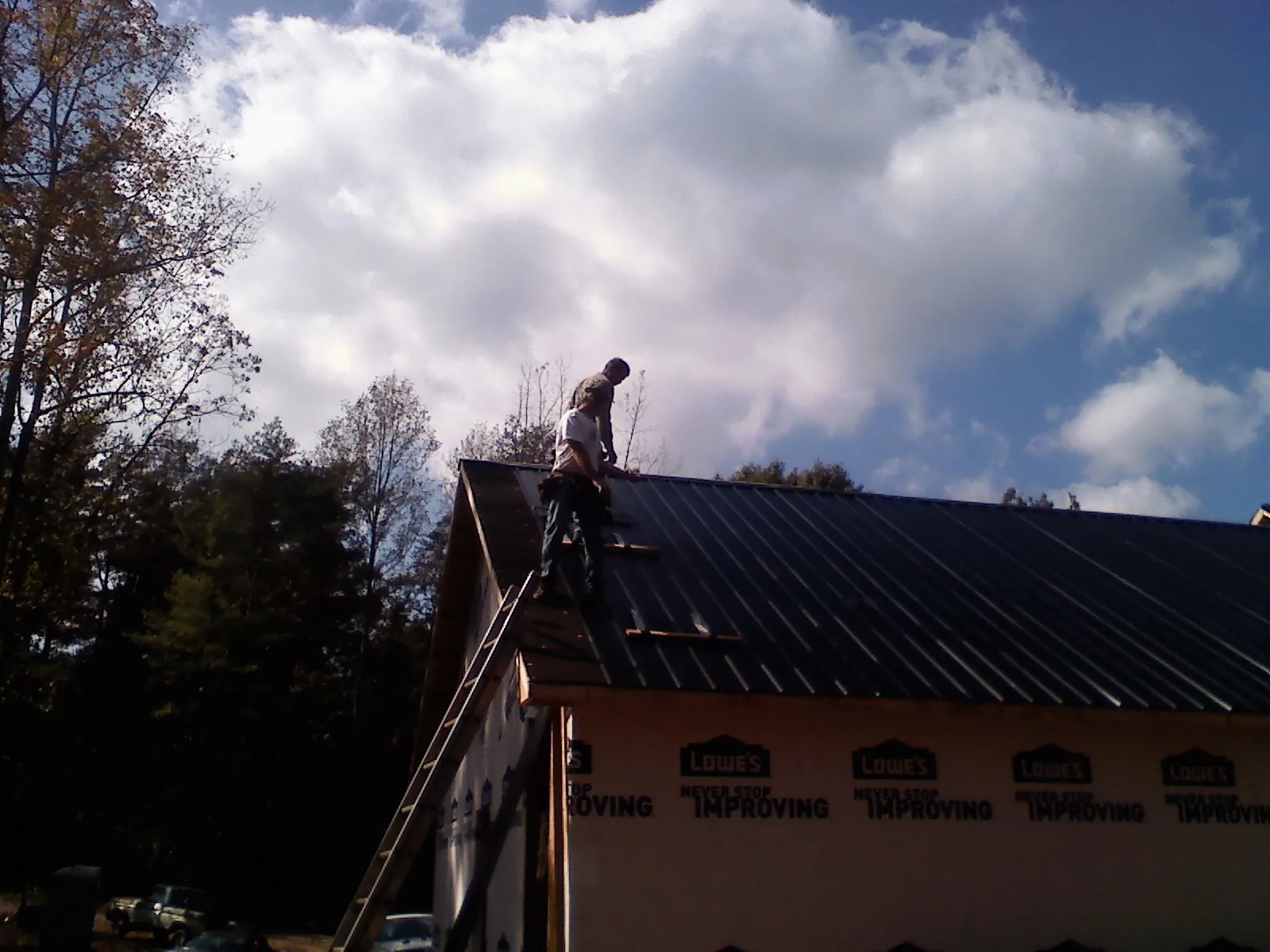 Roofer fastening dark metal panels high against a cloudy sky in Sharpsburg