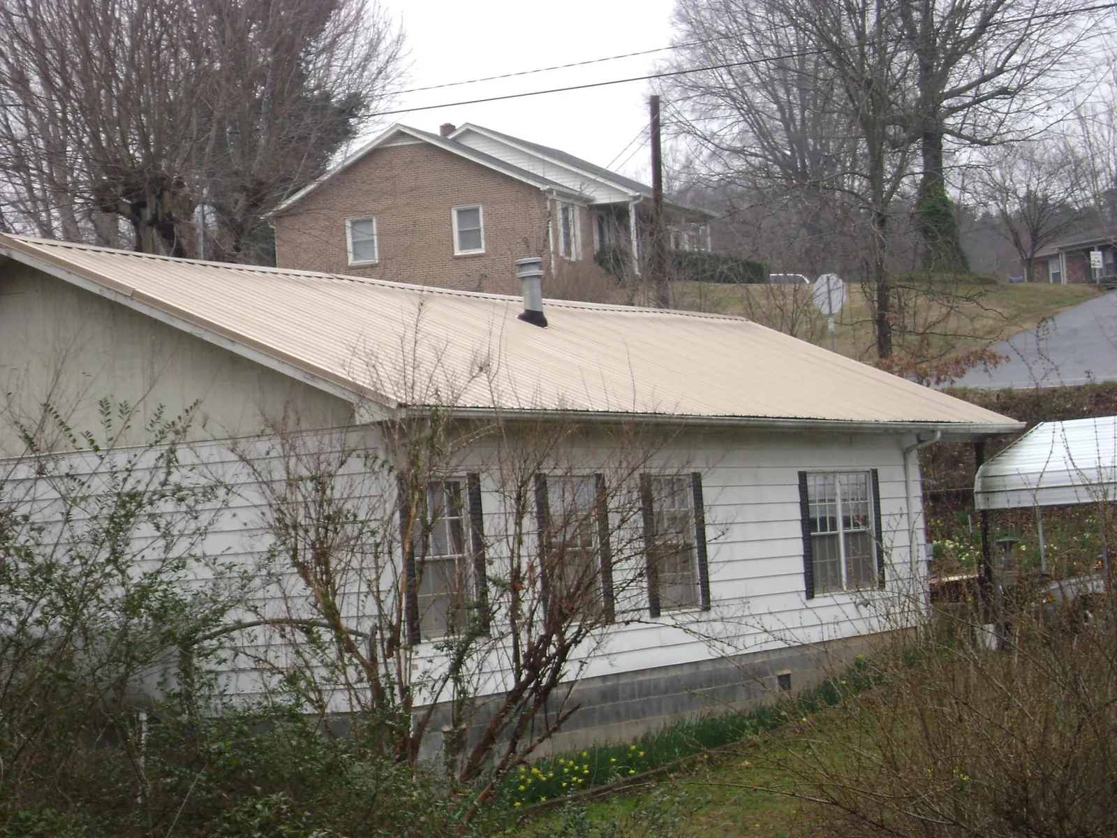 Tan metal roof on a white sided house set into a hillside — Commercial Roofing by Roofing Brothers in Sharpsburg